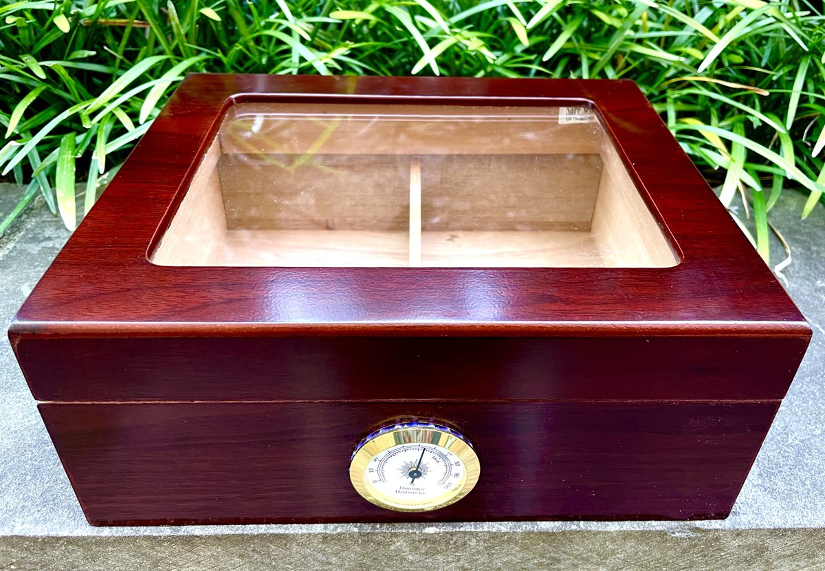 A glass-top desktop humidor, closed, with a hygrometer on the front.